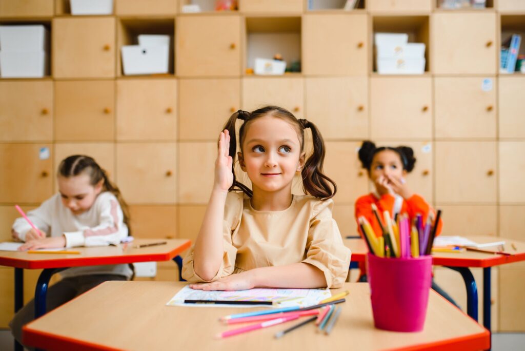 oung girl raises her hand during a lesson in a bright classroom.